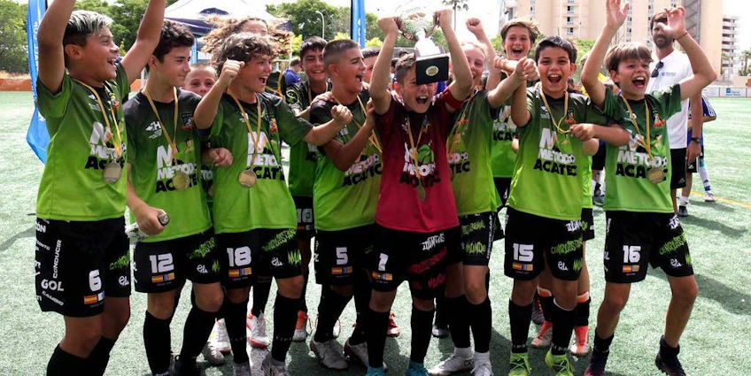 Радостная юношеская футбольная команда с трофеем на праздновании победы на Международном кубке Майорки.