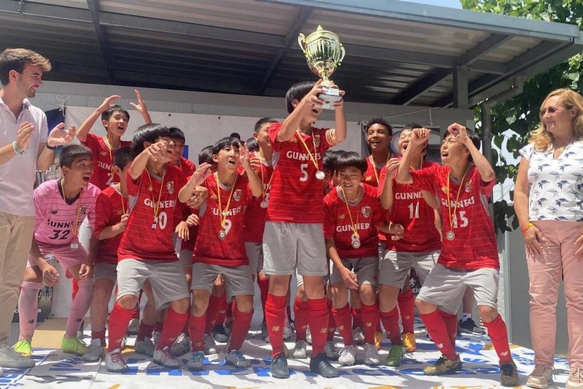 Kırmızı formalı sevinçli genç futbol takımı bir kupayla zaferini kutluyor.