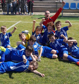 Радостная юношеская футбольная команда в синей форме празднует победу на поле на Кубке Рима.