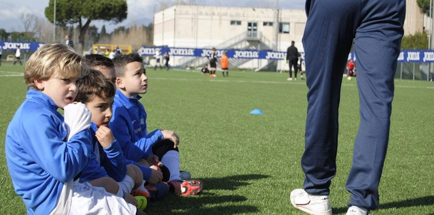 Дети в футбольной форме внимательно слушают тренера на поле