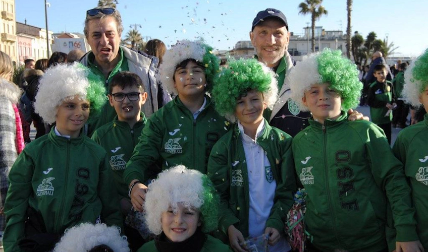 Группа детей в зеленых спортивных костюмах с белыми париками на футбольном турнире