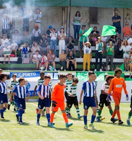 Junior football teams walking onto the pitch with referees and fans in the stands at the Miranda Cup Summer tournament.