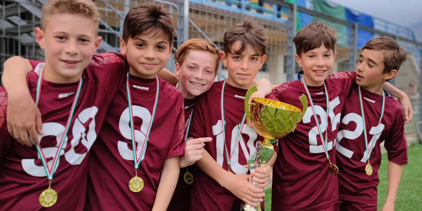 Юные футболисты в бордовой форме с медалями и трофеем на футбольном поле