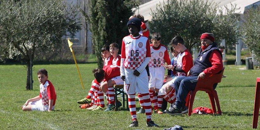 Молодые футболисты в красно-белой форме отдыхают и стратегируют на скамейке запасных во время матча.
