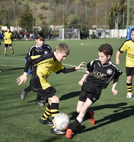 Siyah ve sarı futbol kıyafetleri giymiş çocuklar sahada futbol oynuyor