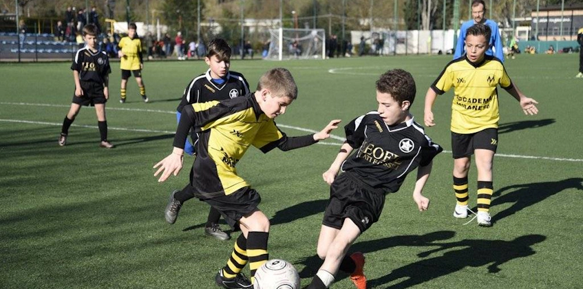 Qara və sarı futbol formalarında uşaqlar meydanda futbol oynayır