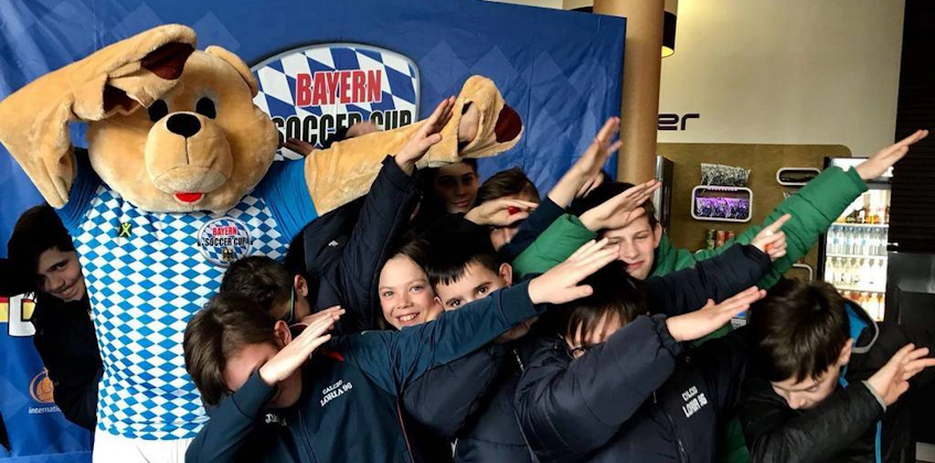 Group of kids with a large plush bear in front of Bayern Soccer Cup logo