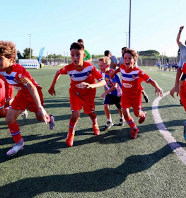 Jovens jogadores de futebol animados em uniformes vermelhos e azuis comemorando no torneio MICFootball 7