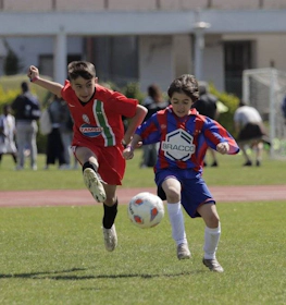 Two young soccer players in red and blue-red jerseys vying for the ball