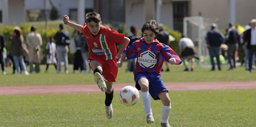 Два юных игрока в футболе в красной и сине-красной форме борются за мяч