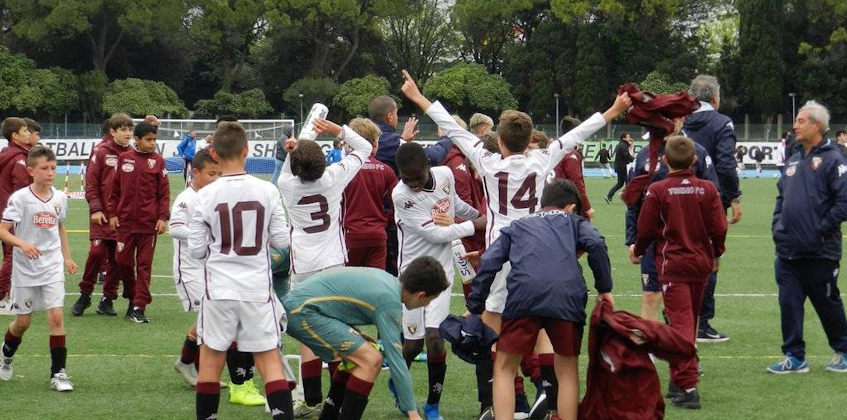 Молодые футболисты празднуют победу на турнире, на заднем плане тренеры и игроки