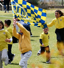 Дети в желтых футболках радостно бегут по футбольному полю с флагами