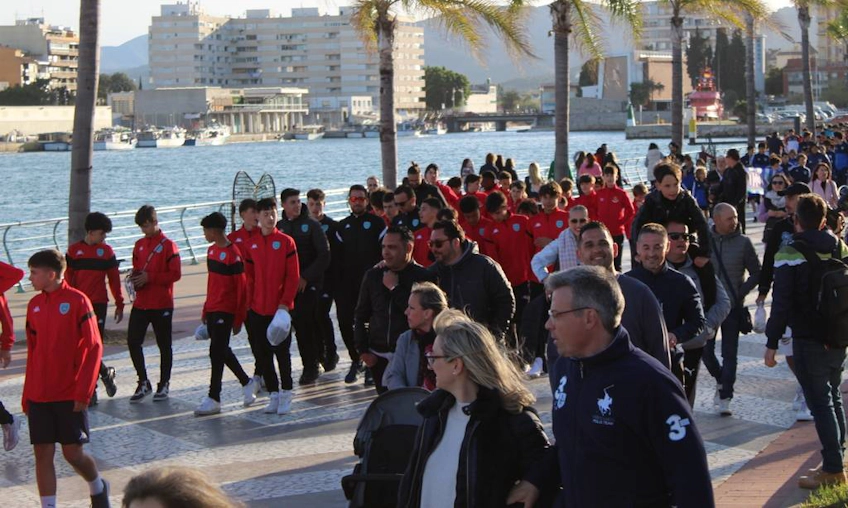 Grupo de equipes de futebol caminhando em um calçadão à beira-mar no torneio Mediterranean Esei Cup