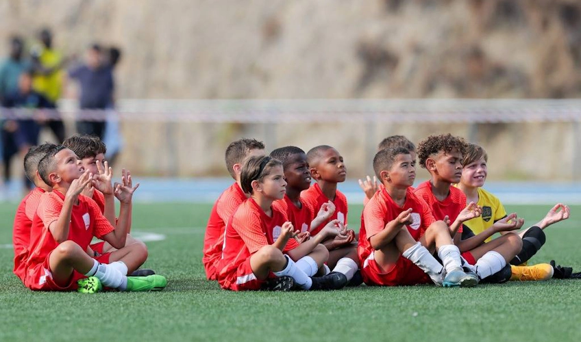 Детская футбольная команда в красных формах сидит на поле на турнире FIT 24 Summer Edition