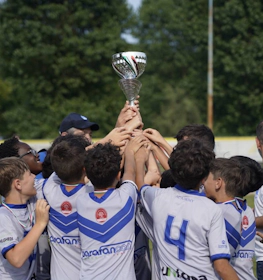 Genç futbolcular futbol sahasında bir kupa kaldırıyor, takımın zafer kutlaması