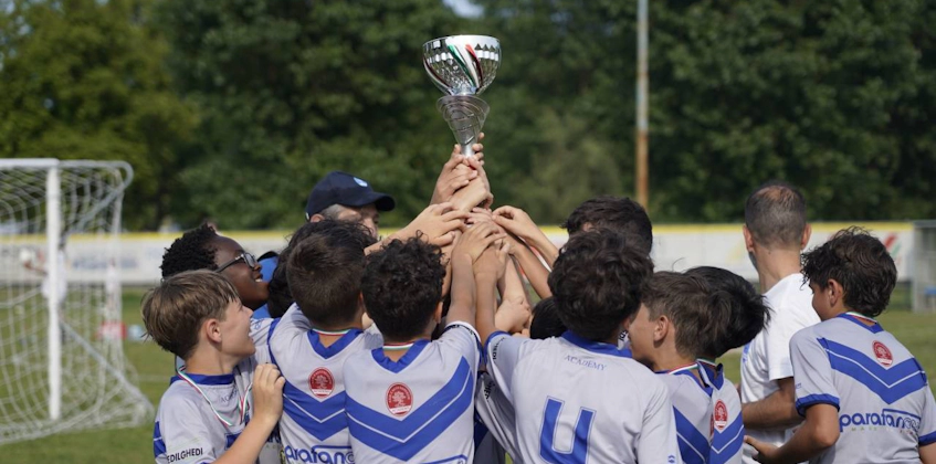 Genç futbolcular futbol sahasında bir kupa kaldırıyor, takımın zafer kutlaması
