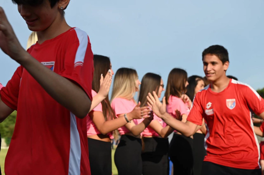 Подростки в красных и розовых футболках радостно приветствуют друг друга на футбольном турнире Trofeo Mar Tirreno