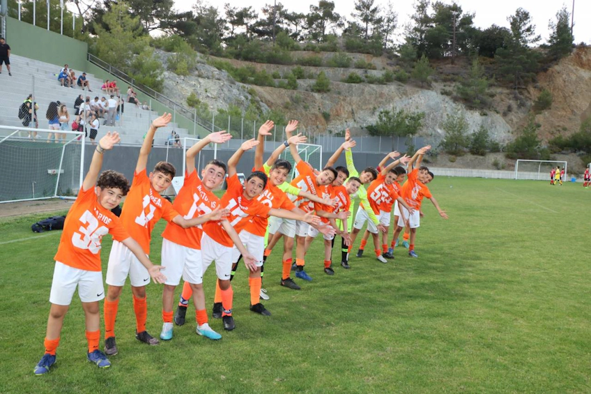 Equipe de futebol juvenil em uniformes laranja comemorando no torneio Platres Football Festival June