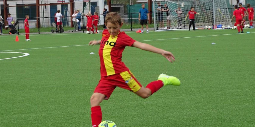 Menino de uniforme vermelho chutando uma bola de futebol no torneio Ixina Cup
