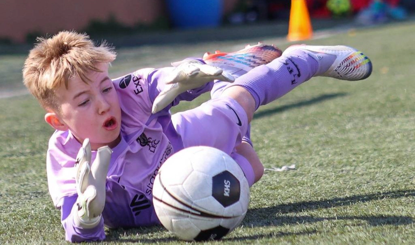 Молодой вратарь в фиолетовой форме делает сейв на футбольном матче