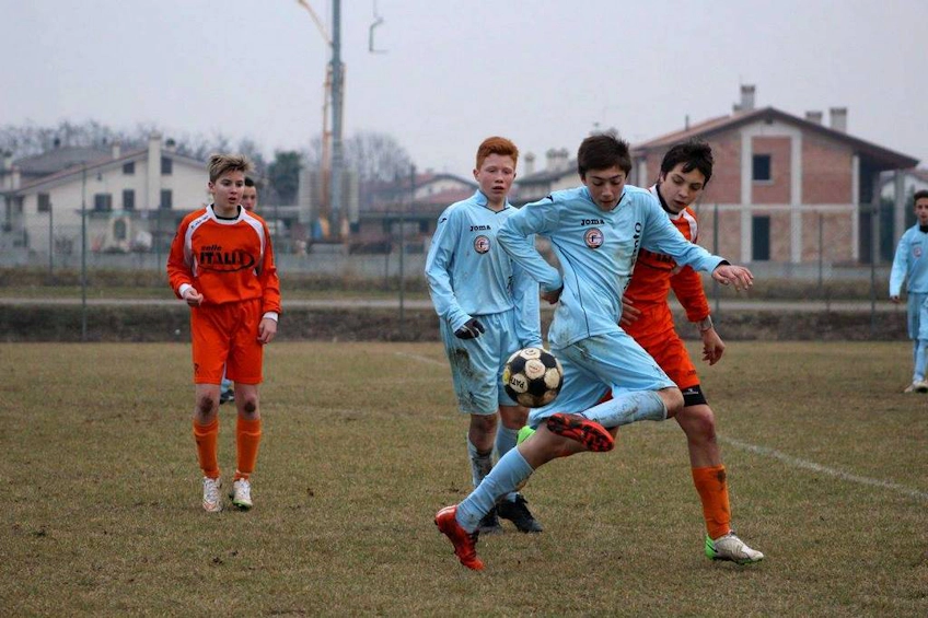 Подростки-футболисты в действии в облачный день, один в светло-голубой форме контролирует мяч.