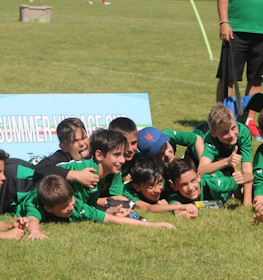 Jovens futebolistas de verde comemoram uma vitória no torneio Summer Village Cup