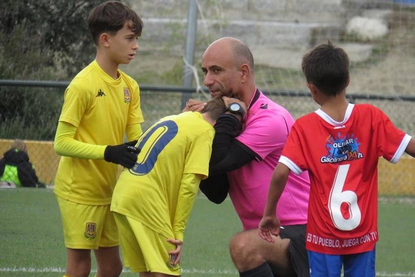Goleiro juvenil de futebol em amarelo conversa com árbitro confortando jogador em vermelho